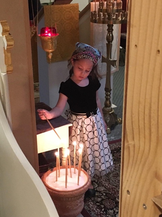 A girl in a headscarf lighting a candle at the candle stand
