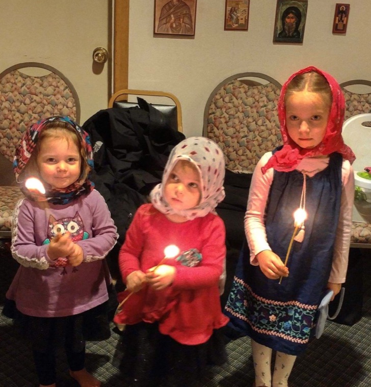 Three small girls in headscarves holding lit candles