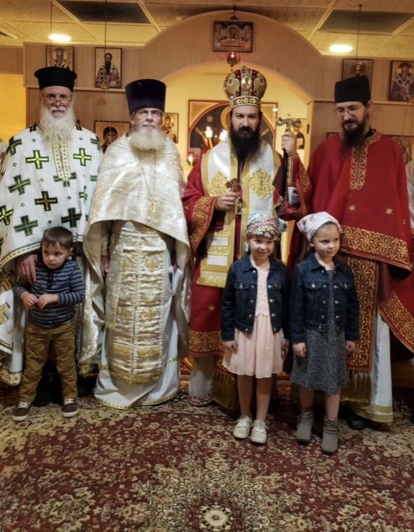 Clergy and the bishop in festal vestments standing with three children of the parish