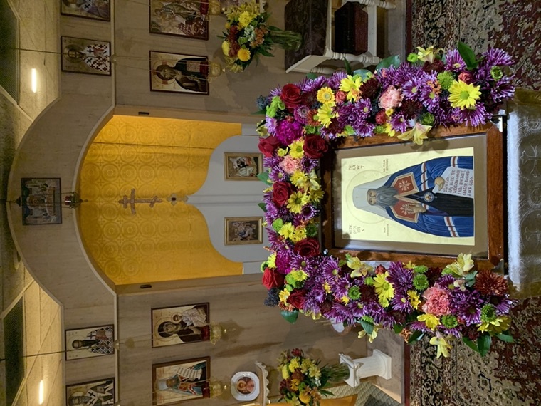 The icon of Saint Philaret on a stand before the altar, ringed by a wreath of purple, yellow and red flowers