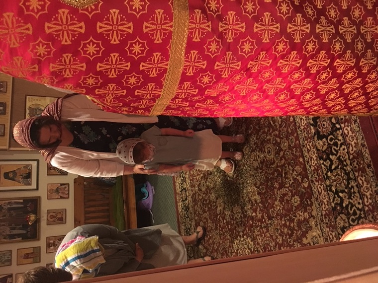 A mother standing with her small daughter in a headscarf on the church carpet