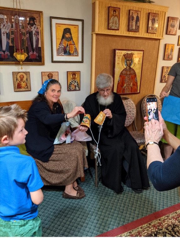 Parishioners seated together in the icon-lined hall, holding painted bells
