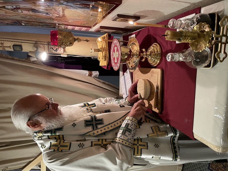 A priest preparing the gifts at the table of oblation, with chalice, diskos and candles