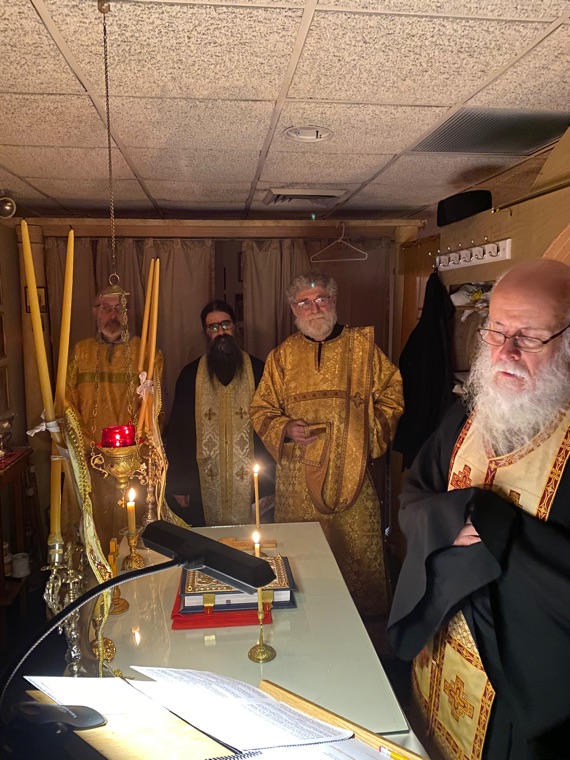 Clergy in gold vestments standing at the altar by candlelight, with tall candles and the Gospel book on the holy table