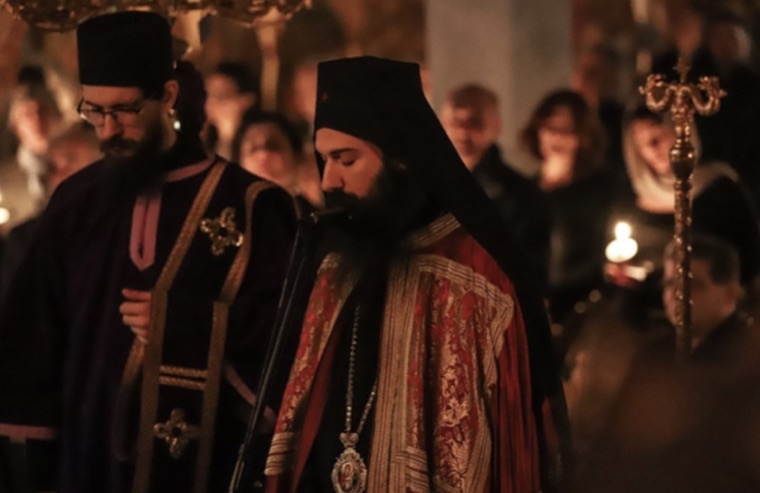 The bishop and a deacon standing in the darkened church during Vigil, lit by candles