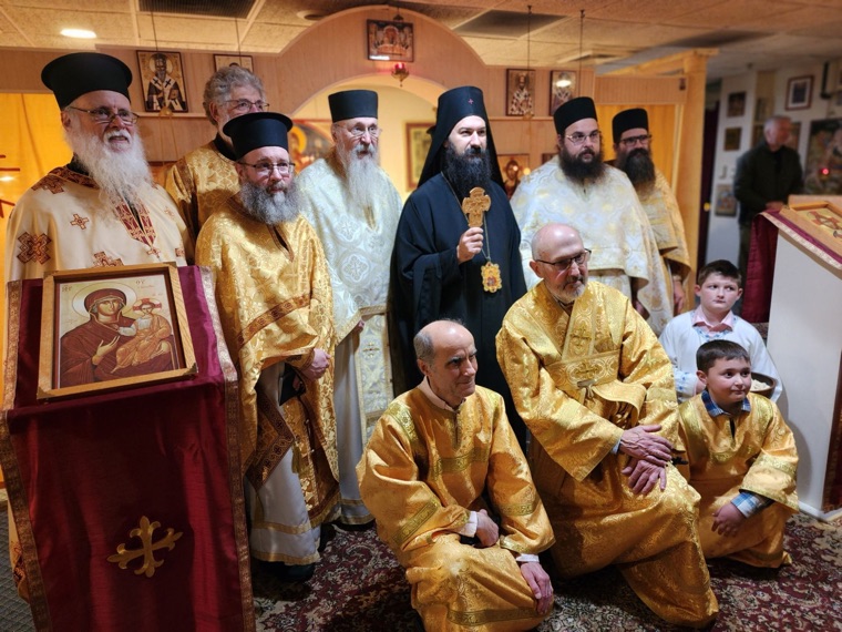 The bishop holding a hand cross among clergy in gold and white vestments, with servers and two boys kneeling in front